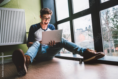 Guy sits on the floor and watches something impressing in laptop