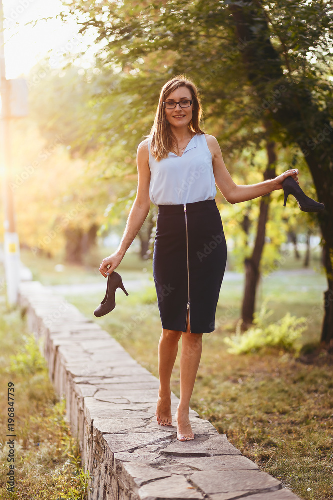 stylish young woman walking barefoot and holding shoes in hand stylish young woman walking barefoot and holding shoes in hand