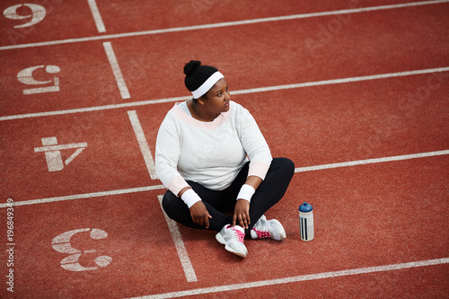 Pensive female in activewear sitting on one of stadium race tracks after training
