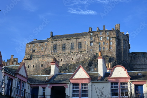 Widok zamku w Edynburgu, Szkocja, na szczycie skalistego wzgórza, na pierwszym planie dachy budynków w Edynburgu, słonecznie, piękne, bezchmurne błękitne niebo