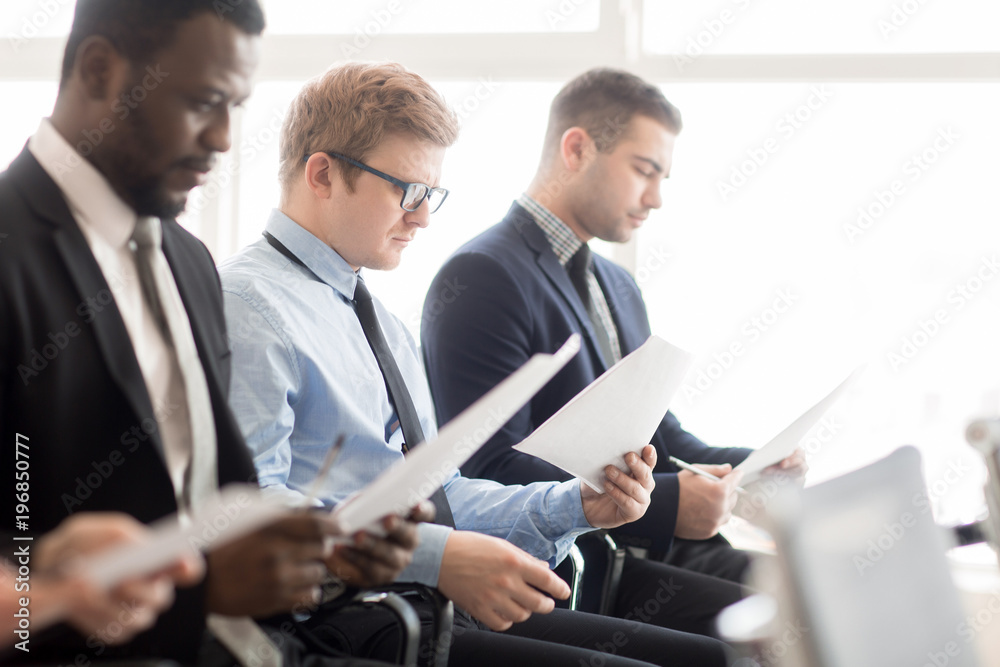 Fototapeta premium Concentrated manager reading attentively information in document among his colleagues at conference
