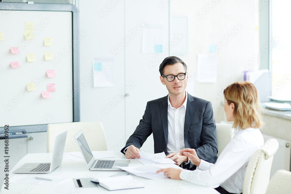 Young confident agent and his colleague having discussion of some documents at meeting Young confident agent and his colleague having discussion of some documents at meeting