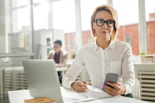 Middle-aged pretty business woman working at smartphone in office