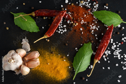 Food and drink healthy lifestyle concept. Spices of chili, black and white sea salt, pepper, basil leaves, turmeric, paprika, garlic on a black stone background © Bera_berc