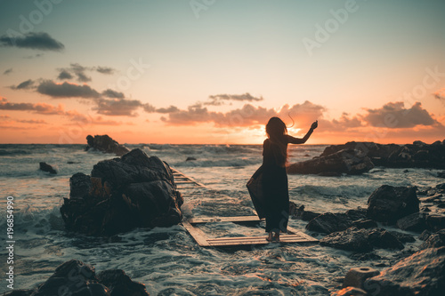 Ragazza in riva al mare danza allegramente al tramonto vicino gli scogli