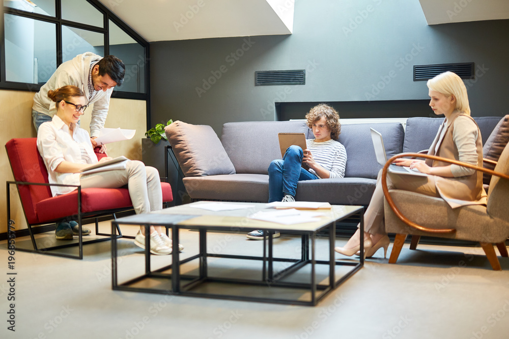 Obraz premium Young creative specialists discussing papers in office with two colleagues working near by