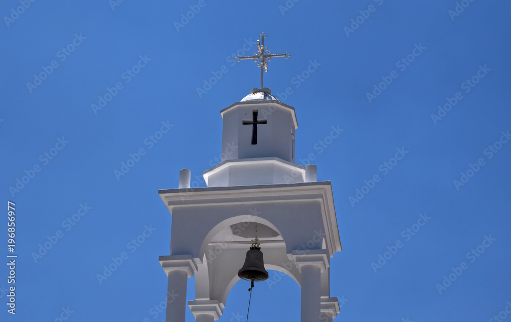 Tower of Holy Monastery of Saint Philimon. White tower with a metallic cross and bell at the Holy Monastery of Saint Philimon. Blue sky background. Tower of Holy Monastery of Saint Philimon. White tower with a metallic cross and bell at the Holy Monastery of Saint Philimon. Blue sky background.