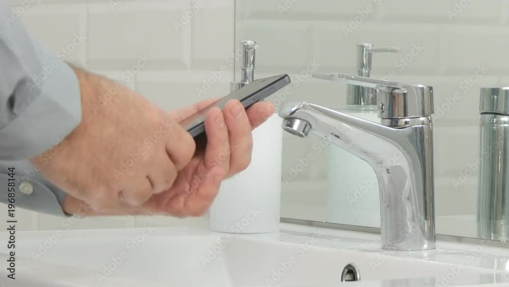 Man Stop Reading Messages on Cellphone and Start Washing His Hands in Bathroom Man Stop Reading Messages on Cellphone and Start Washing His Hands in Bathroom