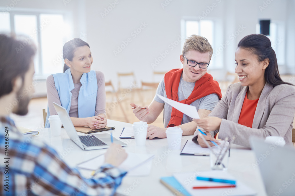 Several young colleagues discussing papers at meeting while sitting by workplace
