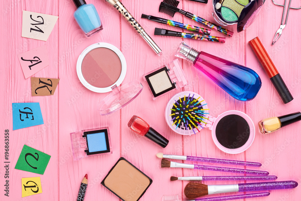 Overhead beauty essentials of modern girl. Female colorful cosmetics and tools, pink background. Paper letters make up. Overhead beauty essentials of modern girl. Female colorful cosmetics and tools, pink background. Paper letters make up.