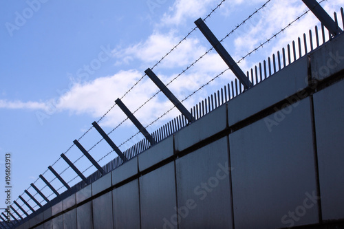 Fotografia Safety wall with barbed wire and spikes on top of a fence provide security - blu