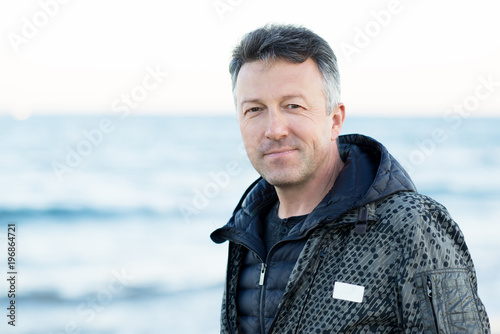 Handsome middle-aged man at the beach. Attractive happy smiling mid adult male model posing at seaside, sunset o sunrise. Outdoor portrait of beautiful man.