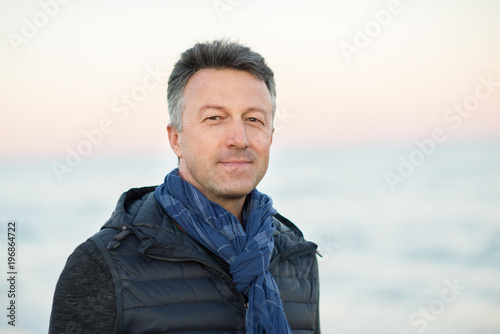 Handsome middle-aged man at the beach. Attractive happy smiling mid adult male model posing at seaside, sunset o sunrise. Outdoor portrait of beautiful man.