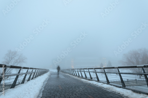 Fototapeta Naklejka Na Ścianę i Meble -  Fuzzy silhouette of a man passing through a pedestrian bridge and reflected in puddles obscure in dense fog . Mystic background