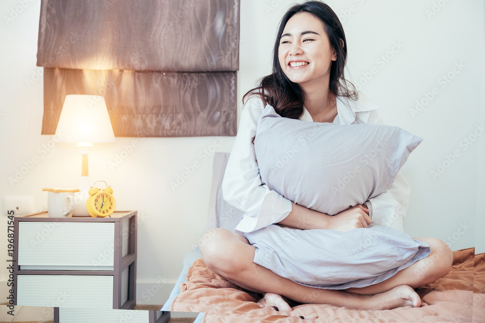 Asian girl who just wake up in the morning as relaxed and smiling. She opened the window to receive the light of the morning sun. She is hugging the pillow after she just wake up. Asian girl who just wake up in the morning as relaxed and smiling. She opened the window to receive the light of the morning sun. She is hugging the pillow after she just wake up.