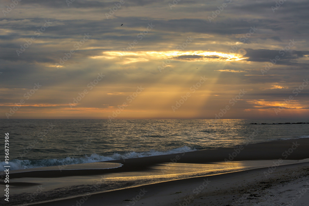 Obraz premium Sun rays cutting thru clouds on to the ocean during golden hour on long island