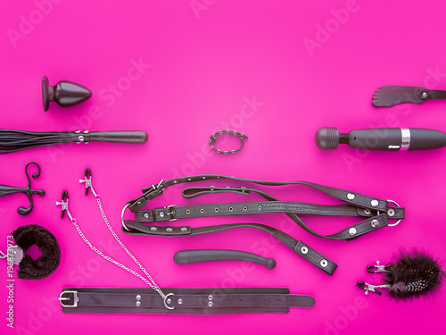 Various toys for adults (leather harness, collar with clips, anal plug, fur handcuffs, vibrator and other) are on a purple background. The image is suitable for the banner of the sex store goods