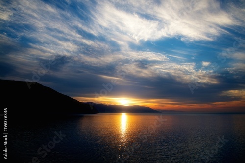 Colored sunset sky with beauty clouds and sun rays. Abstract seascape.