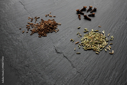 Caraway, fennel seeds and cloves on slate board, copy space