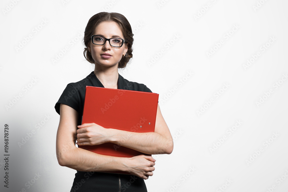 Portrait of confident beautiful young business woman holding binder in her hands standing on grey background Portrait of confident beautiful young business woman holding binder in her hands standing on grey background