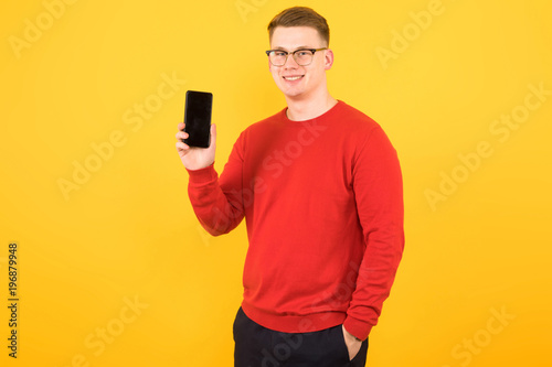 Portrait of young handsome smiling guy holding phone in his hands on yellow background