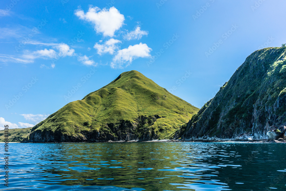 Idyllic seascape from Indonesia with the rock formations of Padar Island reflected in the rippled surface of the sea against a blue sky