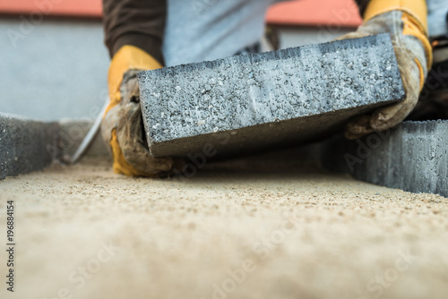 Builder laying a paving brick placing it on the sand foundation photo