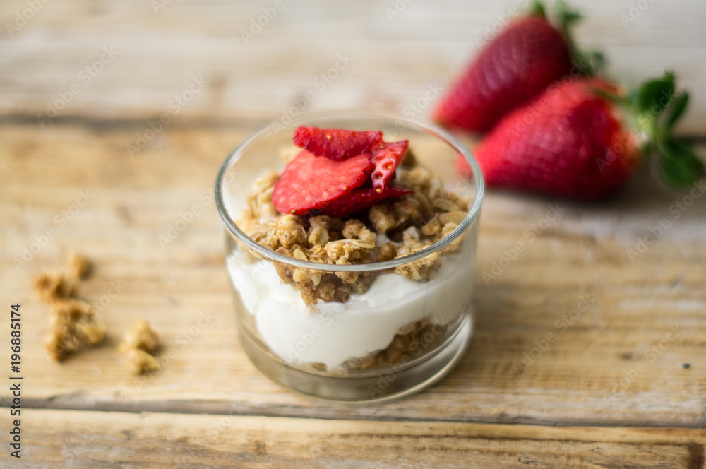 Little glass bowl of homemade granola with greek yoghurt and strawberries, isolated on the wooden rustic table