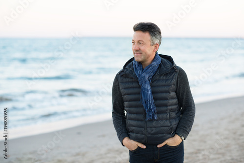 Handsome middle-aged man at the beach. Attractive happy smiling mid adult male model posing at seaside, sunset o sunrise. Outdoor portrait of beautiful man. © Khorzhevska