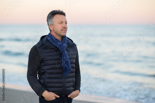 Handsome middle-aged man at the beach. Attractive happy smiling mid adult male model posing at seaside, sunset o sunrise. Outdoor portrait of beautiful man.