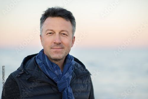 Handsome middle-aged man at the beach. Attractive happy smiling mid adult male model posing at seaside, sunset o sunrise. Outdoor portrait of beautiful man.