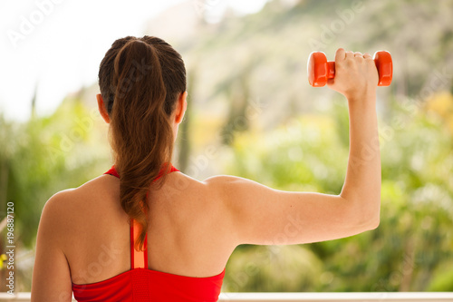 Young athletic woman exercising on verandah: overhead press for upper body strength