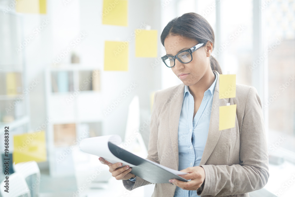 Portrait of a young businesswoman in suit and eyeglasses holding clipboard with documents Portrait of a young businesswoman in suit and eyeglasses holding clipboard with documents