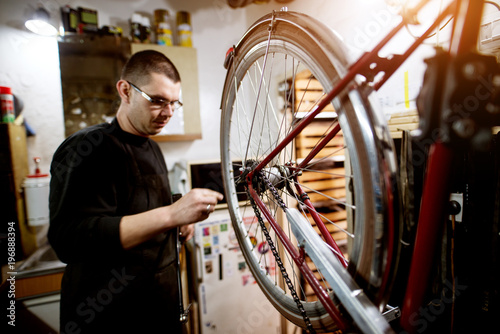 Fototapeta Naklejka Na Ścianę i Meble -  Young guy checking bicycle wheel balance in the garage.
