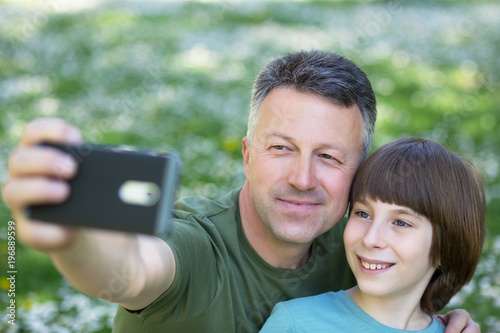Father and son taking photo with smartphone together outdoor. Family selfie time.