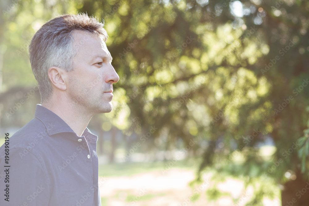 Handsome middle-aged man in park, portrait in profile. Attractive mid adult male model posing outddor. Handsome middle-aged man in park, portrait in profile. Attractive mid adult male model posing outddor.