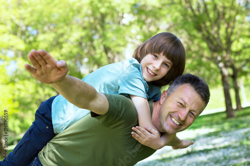 Portrait of father with his son having fun in summer park. Piggyback. Family fun. Happy boy playing with dad summer nature outdoor