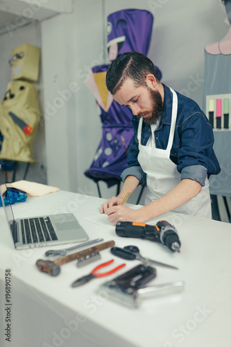 Male designer in the craft workshop working. Young designer drawing on the desk with a laptop and tools