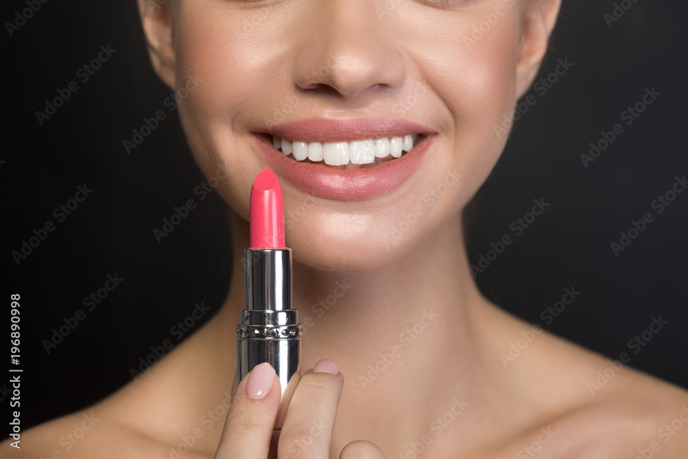 Close up of smiling mouth of optimistic cute girl who is holding pink lipstick. Lip beauty concept Close up of smiling mouth of optimistic cute girl who is holding pink lipstick. Lip beauty concept