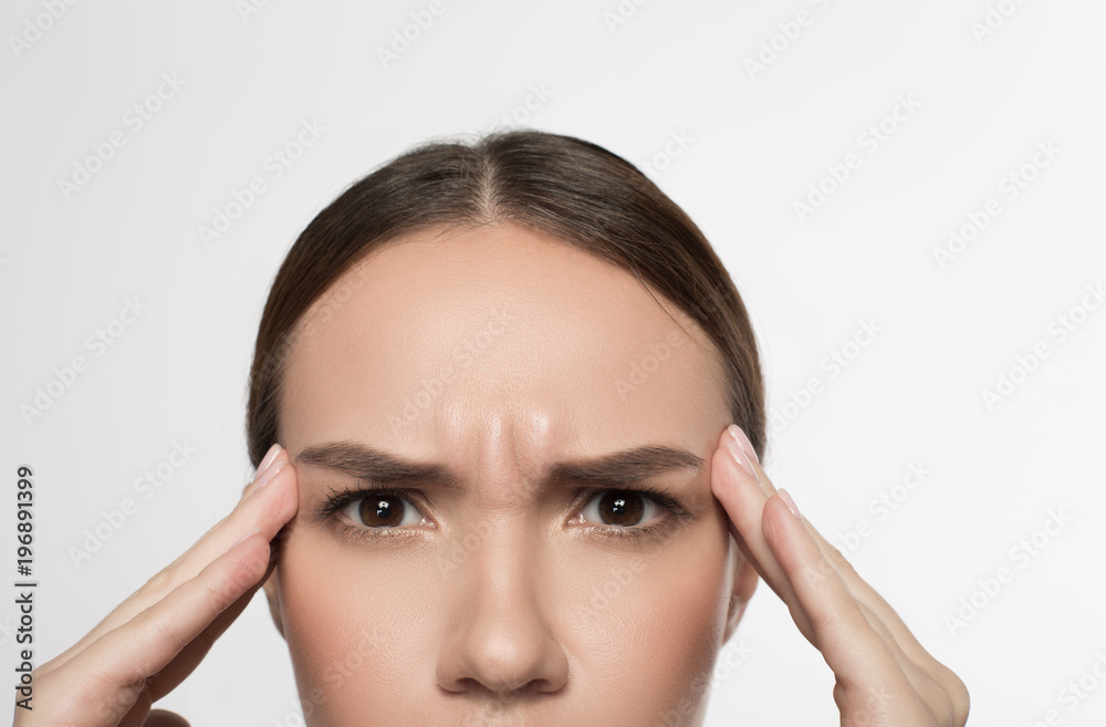 Stressful day. Half of face of unhappy girl is holding her hands on temples while feeling headache. She is looking at camera with suffer. Isolated background Stressful day. Half of face of unhappy girl is holding her hands on temples while feeling headache. She is looking at camera with suffer. Isolated background