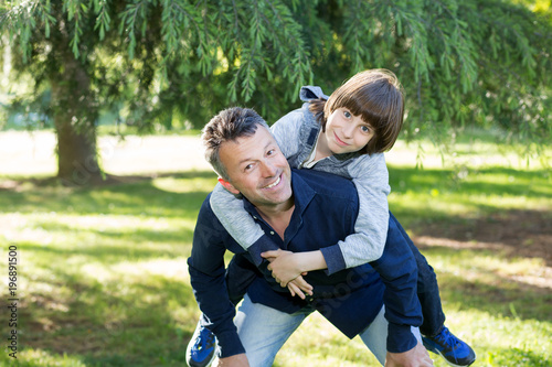 Portrait of father with his son having fun in summer park. Piggyback. Family fun. Happy boy playing with dad summer nature outdoor. Parenting. Two generations.