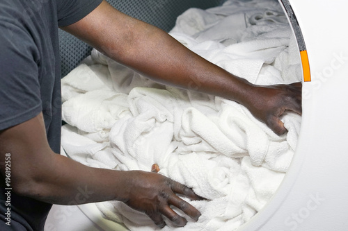 The hands of an african male laundry worker in the inn give a clean towel from the washing machine. Washing machine in stylish hotel laundry. Laundry in the hotel.