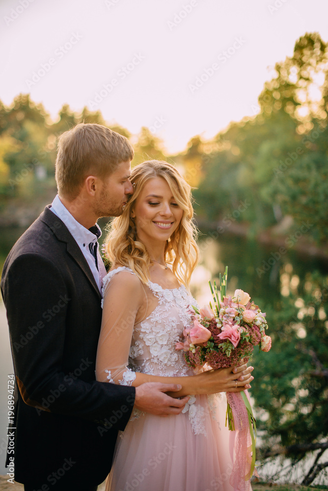 groom kisses a happy bride against the backdrop of nature at sunset