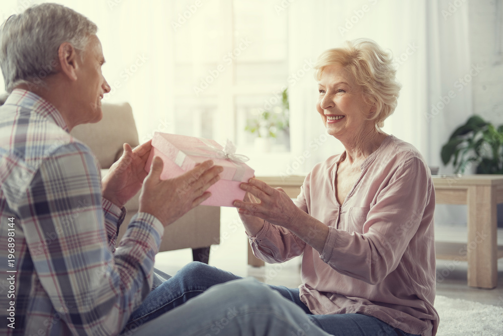 Retired married people sitting on the floor at home. Husband giving surprise to his wife Retired married people sitting on the floor at home. Husband giving surprise to his wife