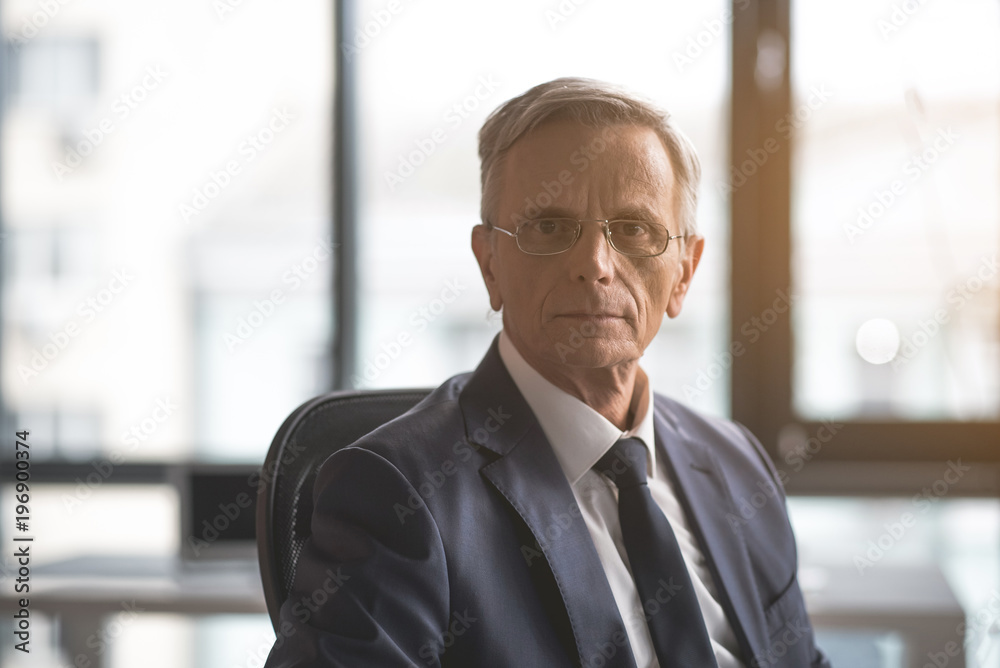 Portrait of serene old businessman watching at camera while working indoor. Calm employer during occupation concept Portrait of serene old businessman watching at camera while working indoor. Calm employer during occupation concept