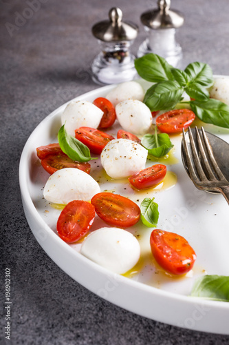 Delicious caprese salad with ripe cherry tomatoes and mini mozzarella cheese balls with fresh basil leaves. Italian healthy food concept with copy space.