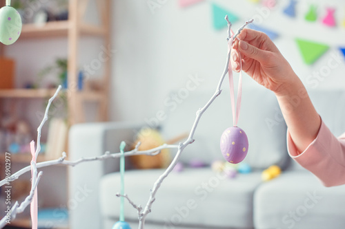 Canvas Print Young woman at home easter celebration concept hanging egg on tree
