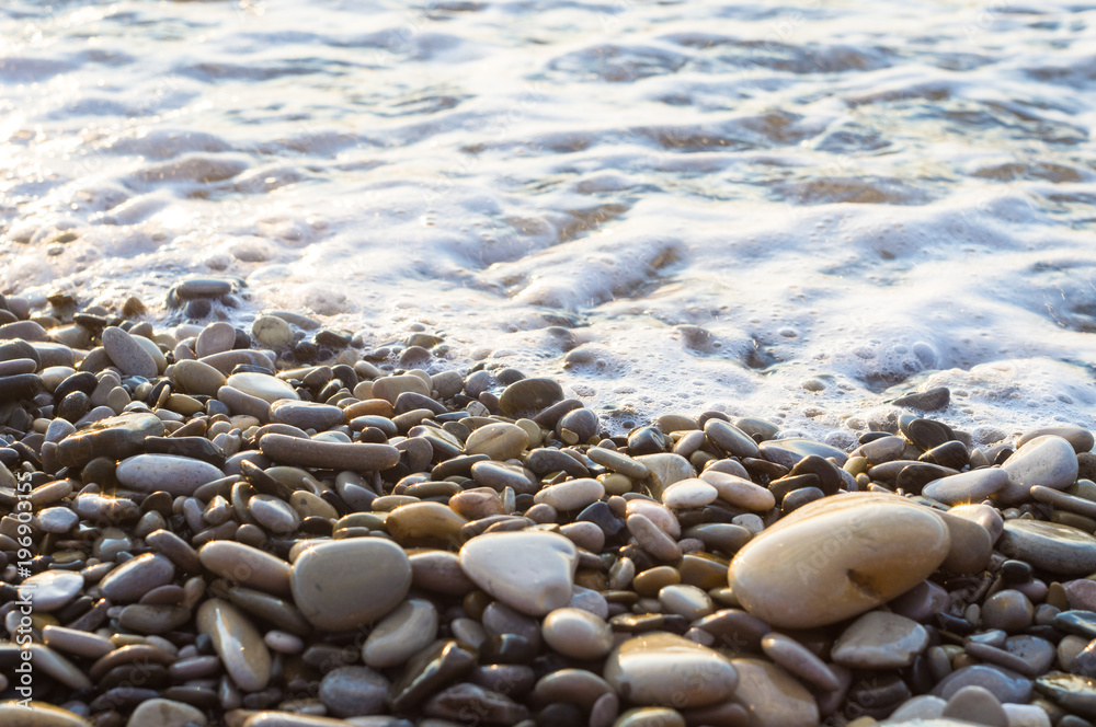 pebble stones on the sea beach, the rolling waves of the sea with foam