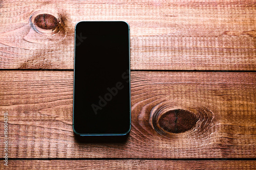 Top view of a modern smartphone with large screen on vintage wooden table. Blank empty display
