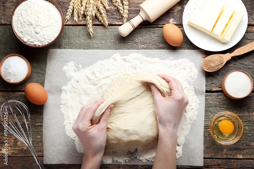 Fotografi female hands knead dough and butter on plate with eggs on wooden table